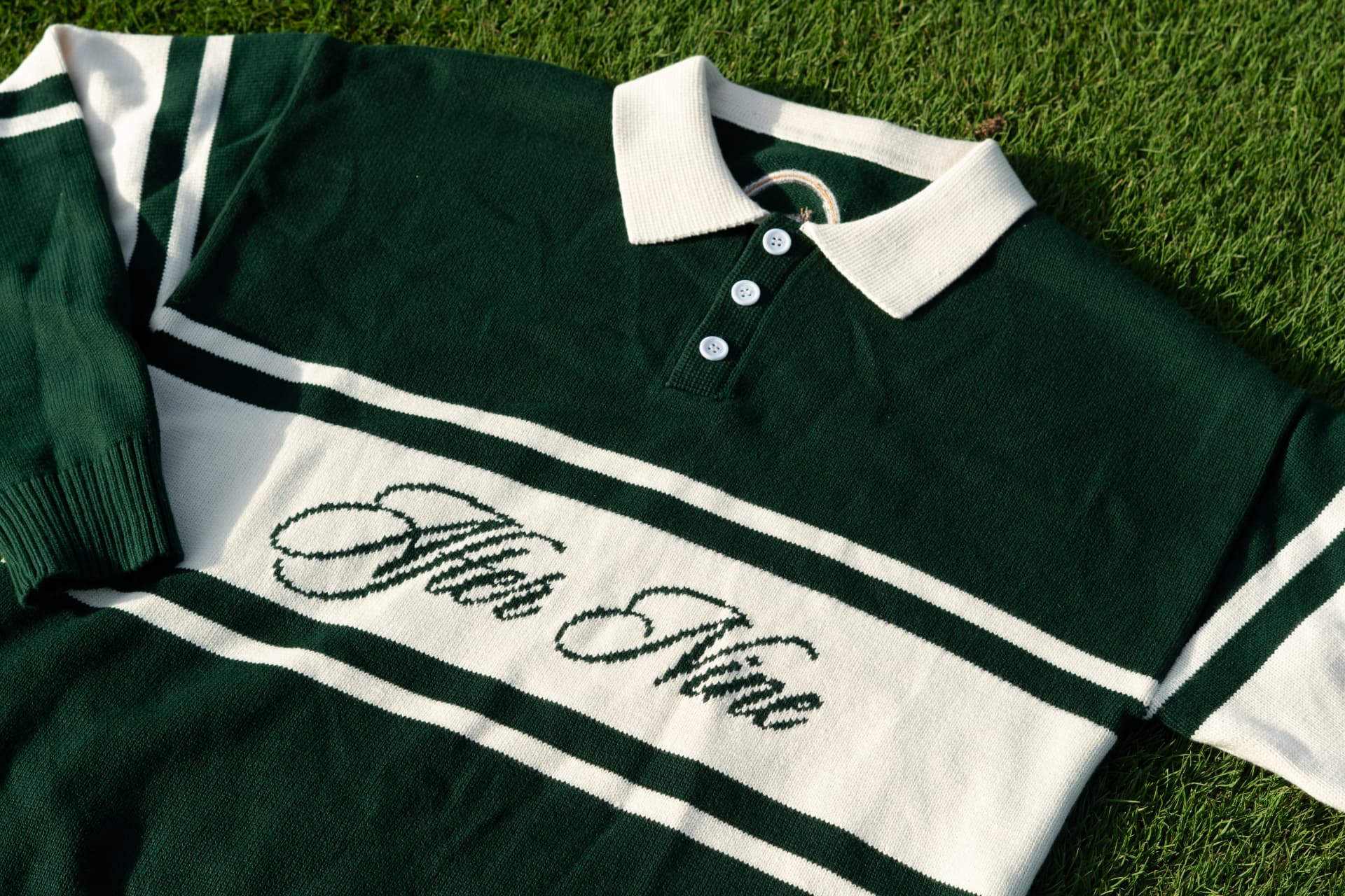Knit polo with striped cuffs and collar laid flat on a sunlit golf green