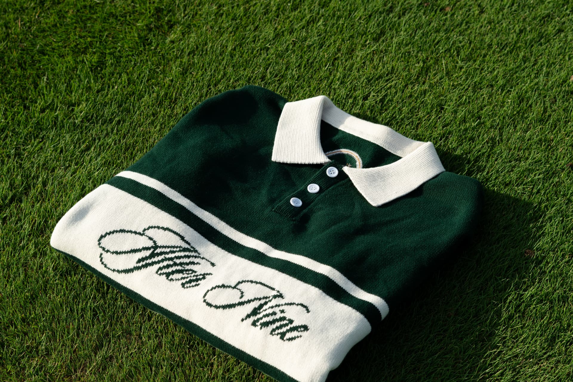 Folded cream and forest-green knit polo resting on a sunlit golf green